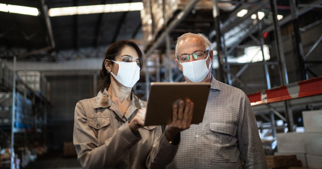 Senior partners walking and using digital tablet at warehouse - with face mask