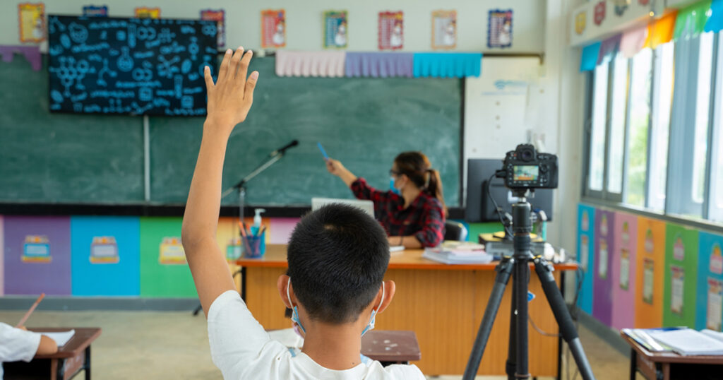 School kids wearing protective mask to Protect Against Covid-19,Group of school kids with teacher sitting in classroom online and raising hands,Elementary school,Learning and people concept.