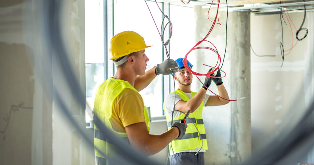 Side view at two construction crew workers separated by wall while renovating house, copy space. portrait of young people electrician connecting cables in wires cabinet while renovating house, copy space